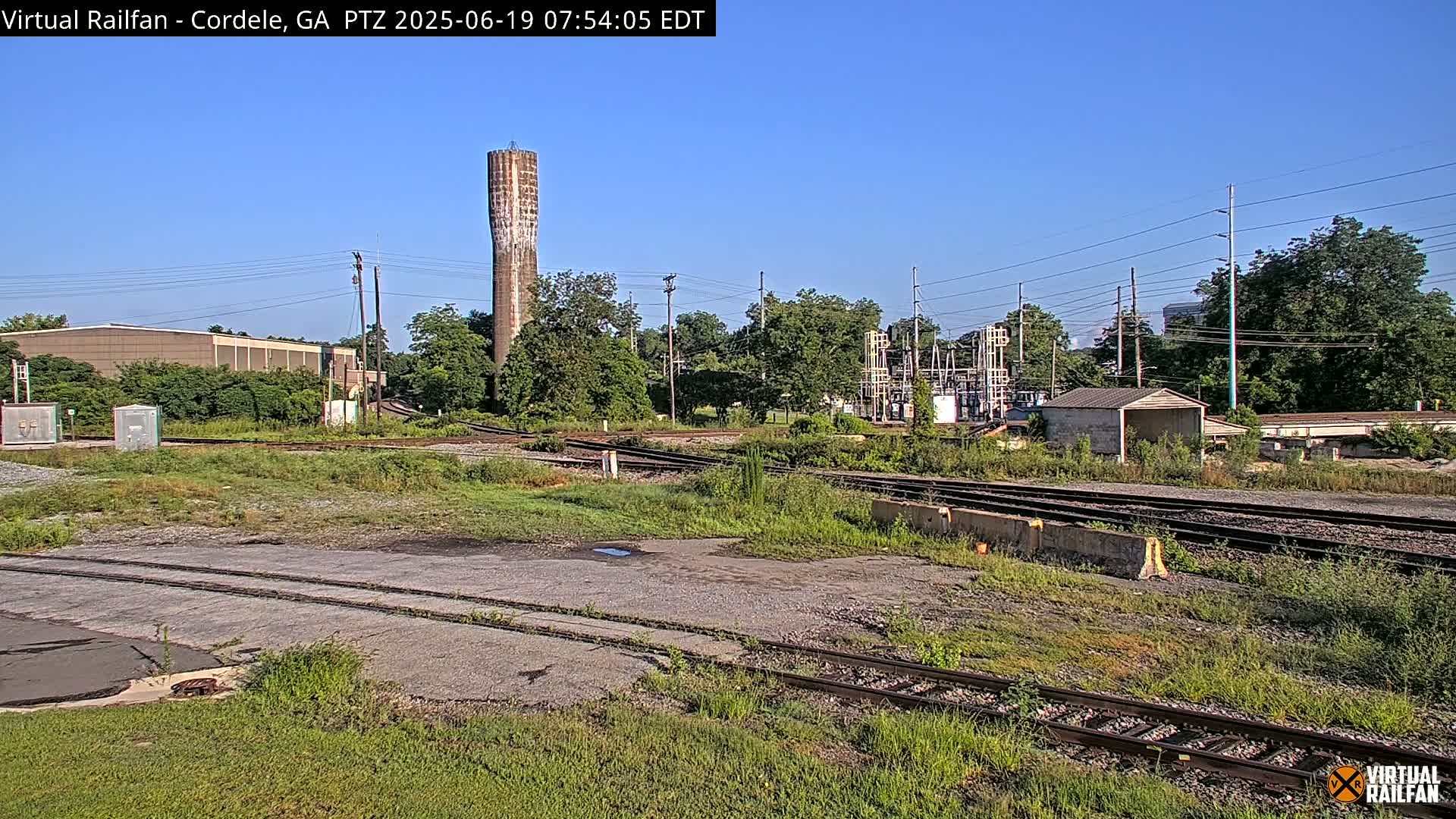 A railway switching yard with a tall water tower in the background on a sunny day.