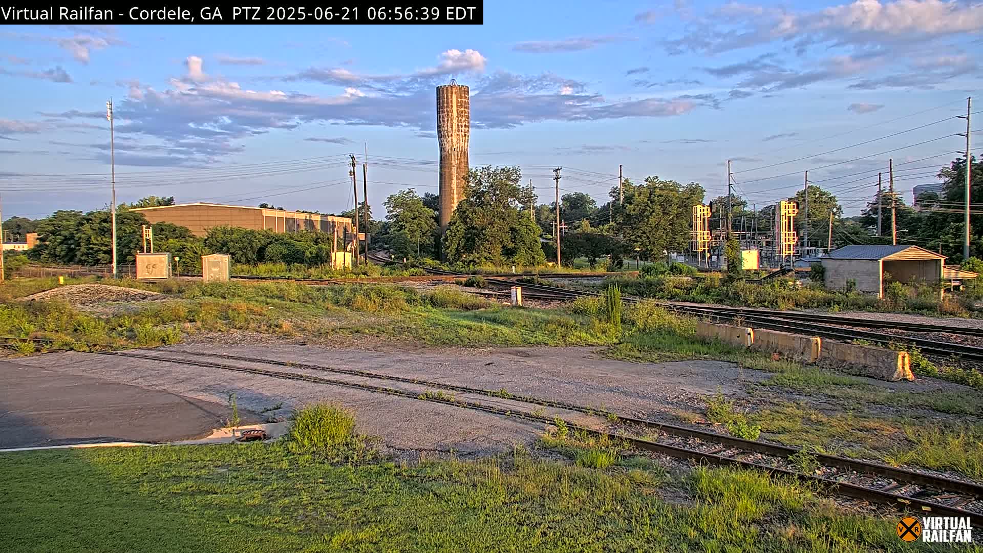 A tall, slender water tower is visible in the distance behind a railway switching yard under a partly cloudy, twilight sky.