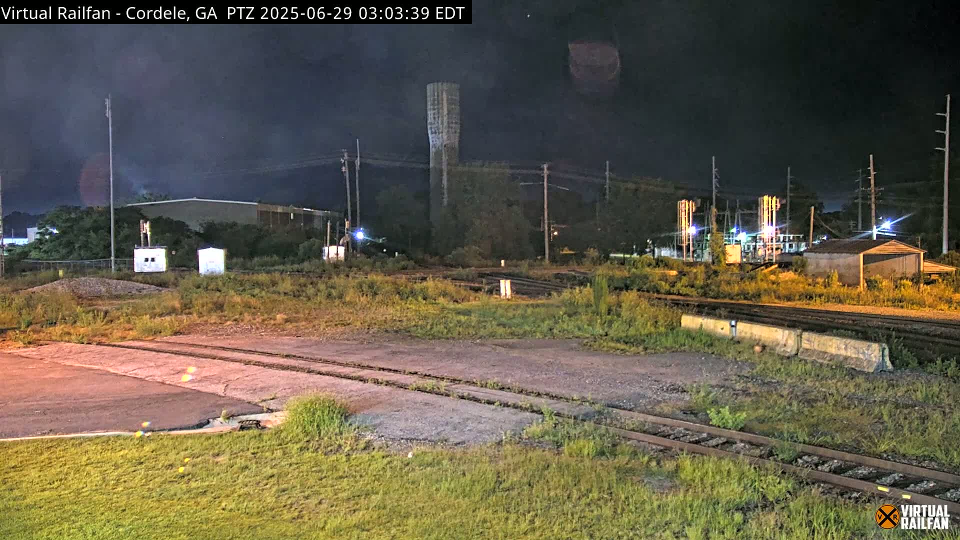 A nighttime view of a rail yard with a tall tower in the background, under a dark sky.