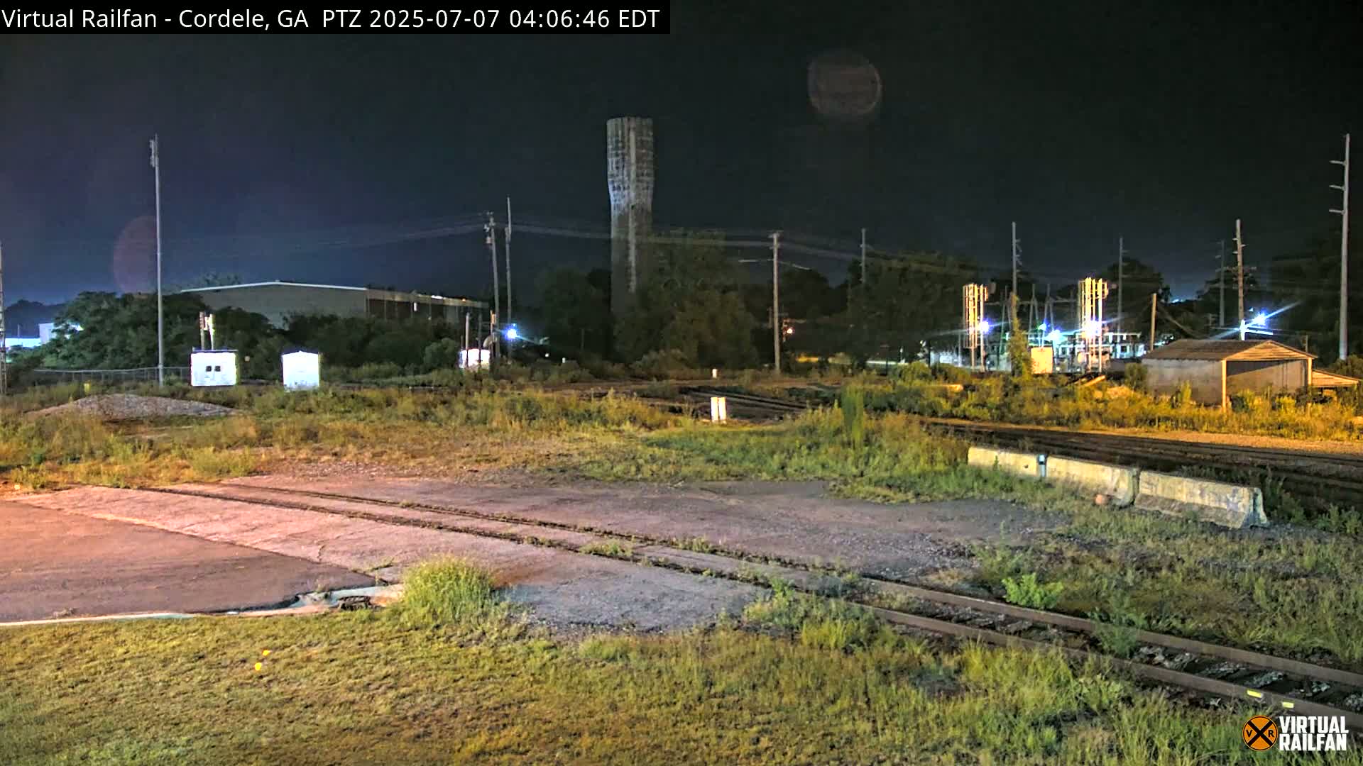 A nighttime view of a rail yard with a water tower in the background under a dark, clear sky.
