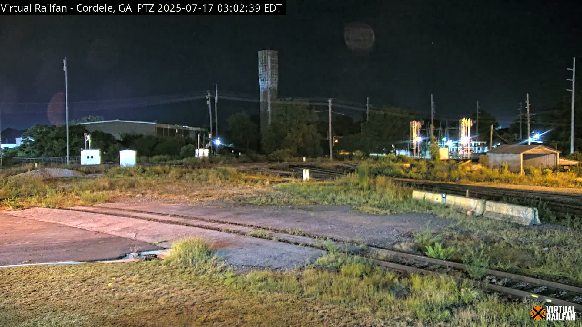 A nighttime view of railroad tracks, adjacent buildings, and a tall water tower under a dark, clear sky.
