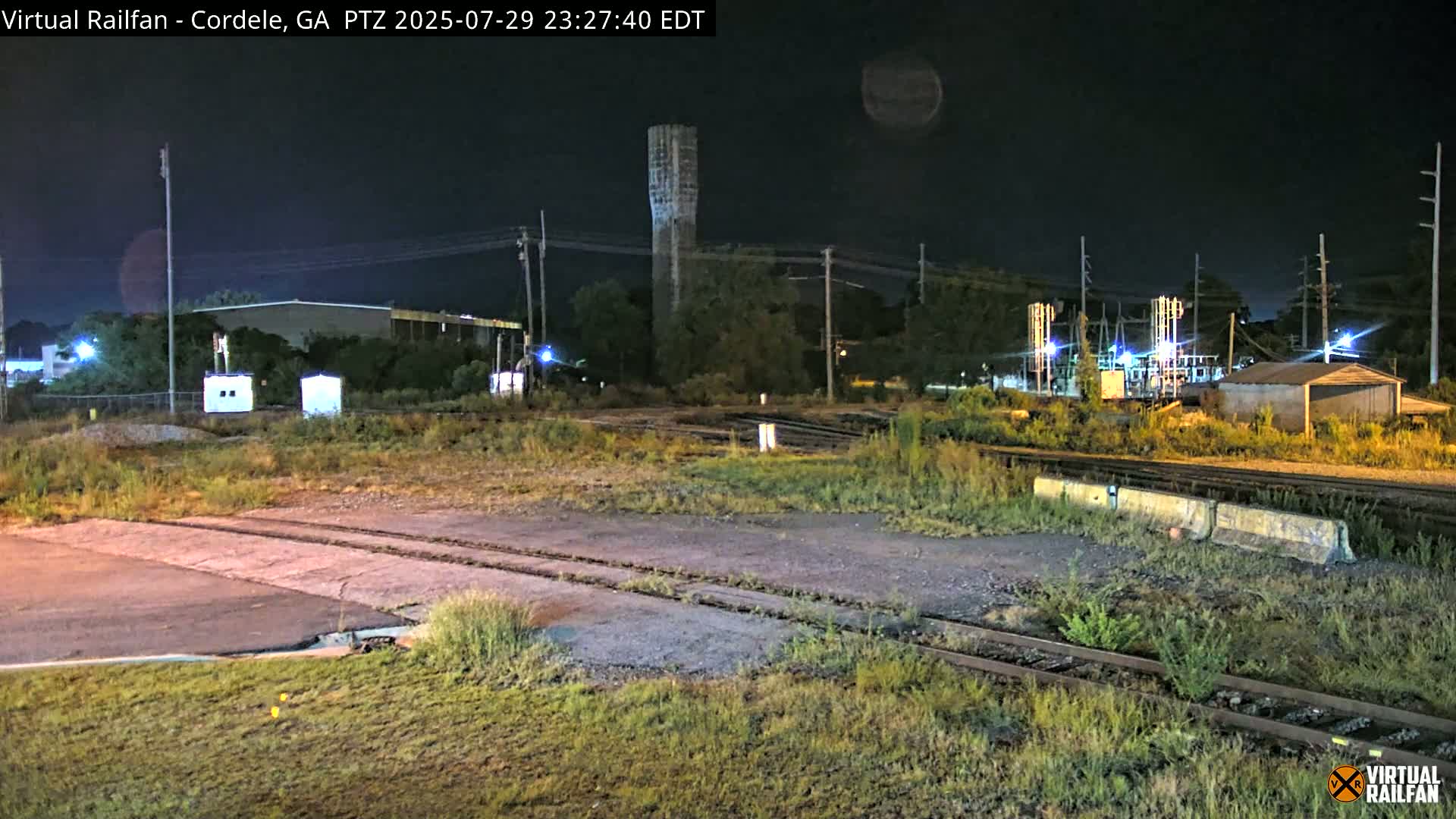 A nighttime view of a railroad yard with a water tower in the background under a clear, dark sky.