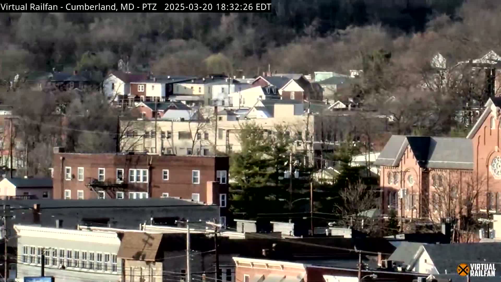 A long shot of a residential area with brick buildings and trees, on a partly sunny day.