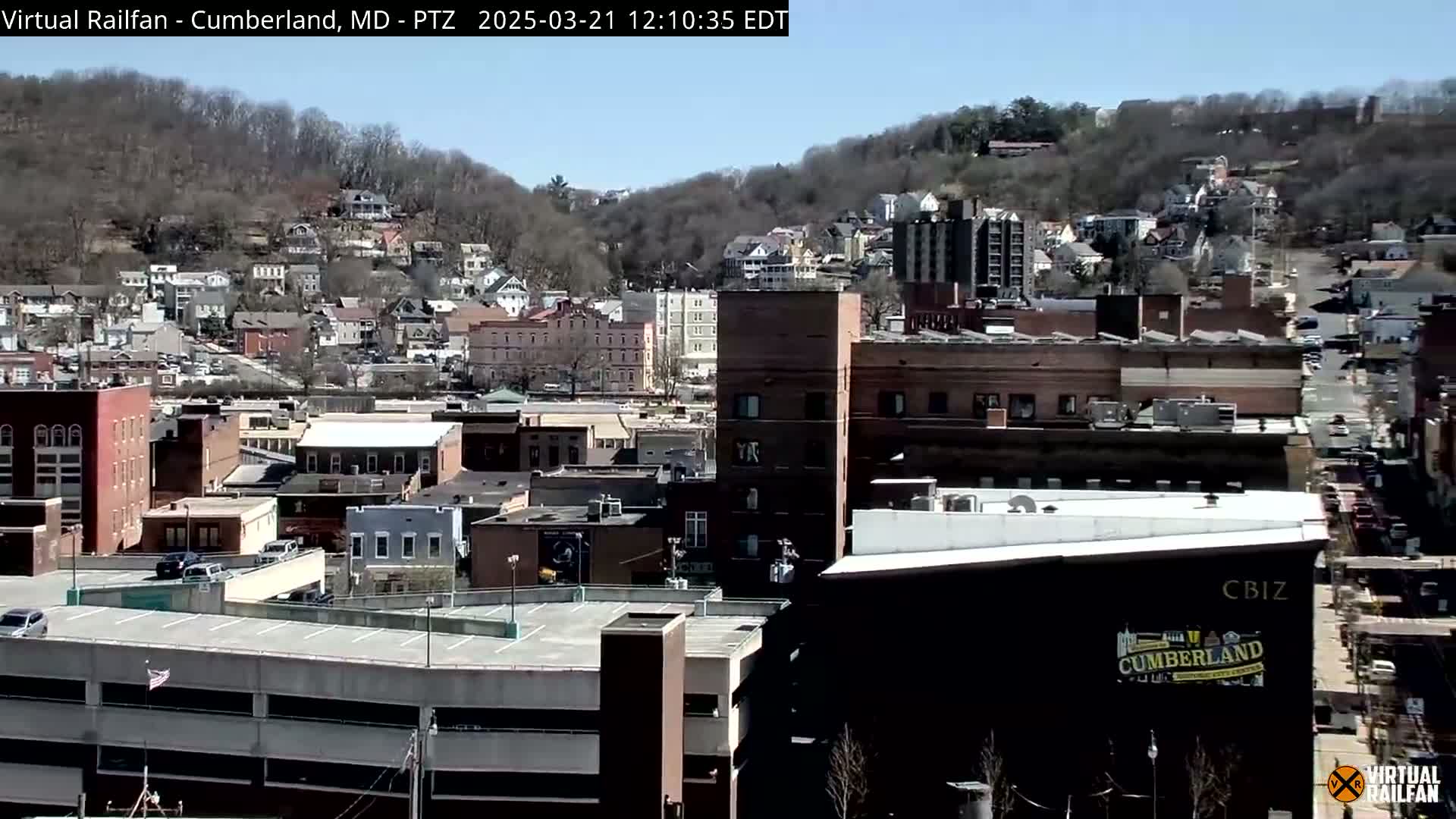 A city scene on a clear, sunny day, showing a mix of residential and commercial buildings nestled against a hillside.