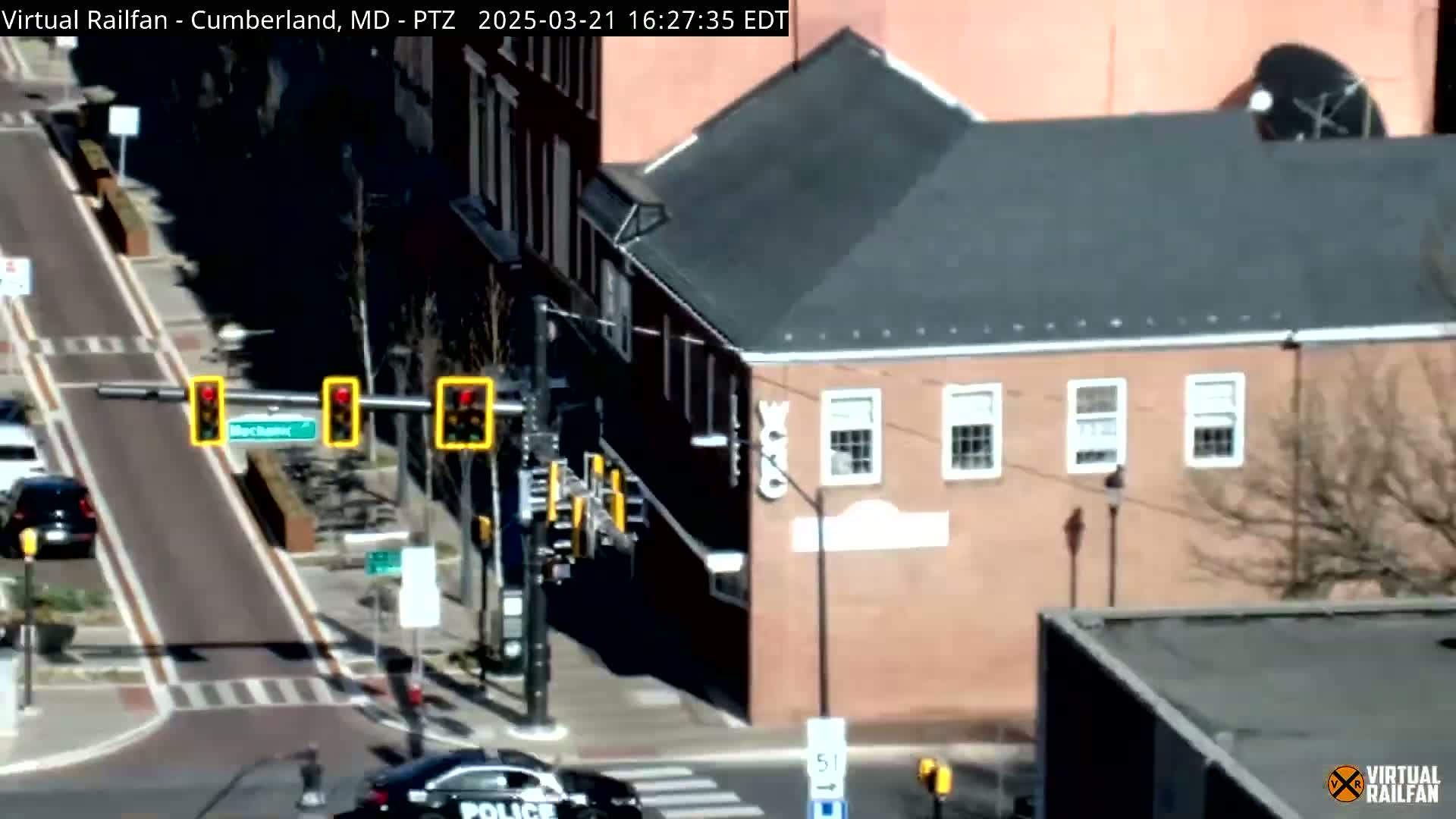 A sunny day shows a street intersection with a police car, traffic lights, and brick buildings; a bike lane is visible.