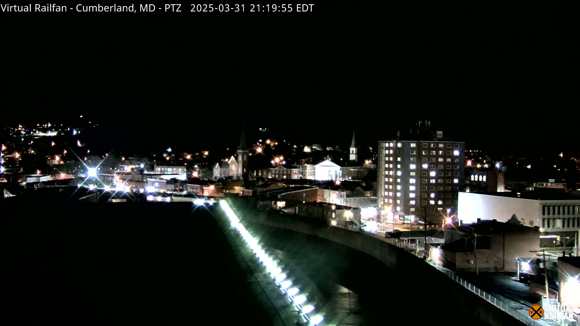 A nighttime view of a city illuminated by streetlights, featuring a canal or river with lights lining its edge.