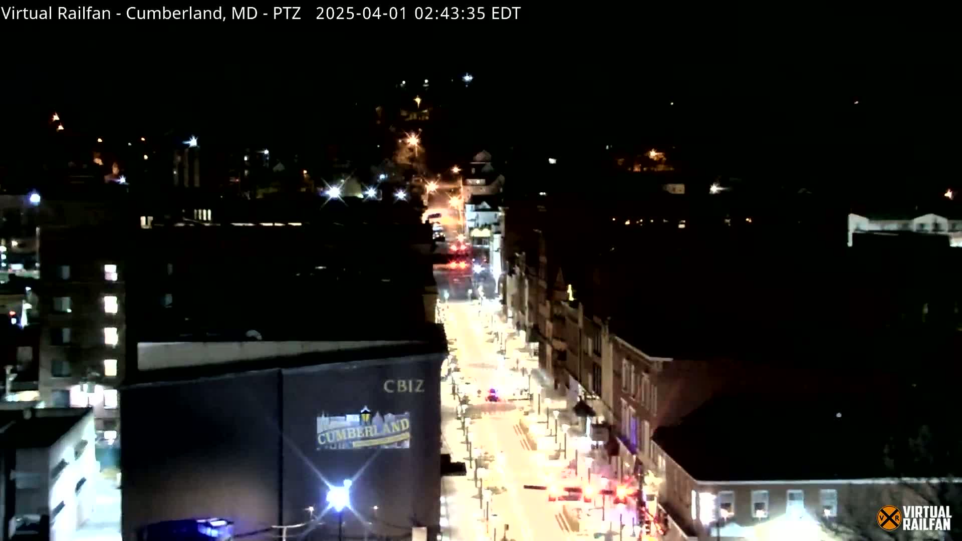 A nighttime aerial view of a city street with sparse vehicle traffic and illuminated buildings.
