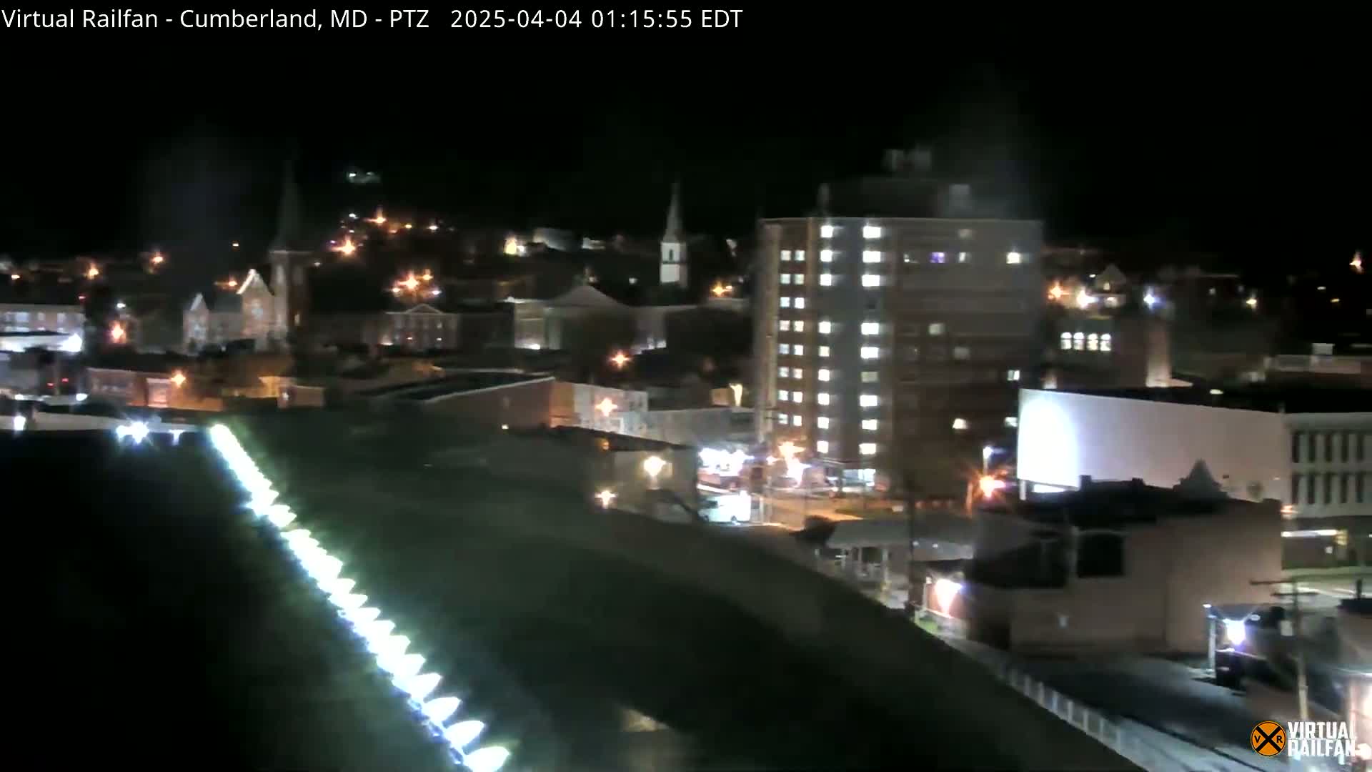 A nighttime view of a city with illuminated buildings, streets, and a long line of lights on the ground.