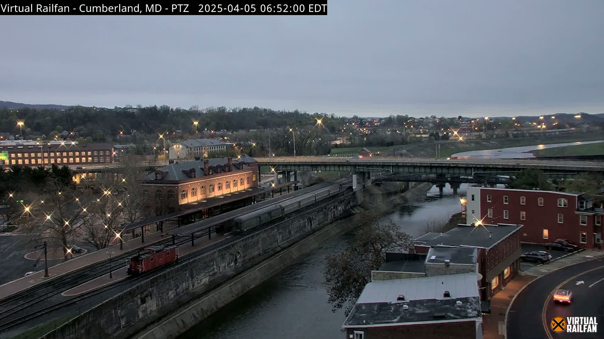 A train sits at a station beside a river under a twilight sky.