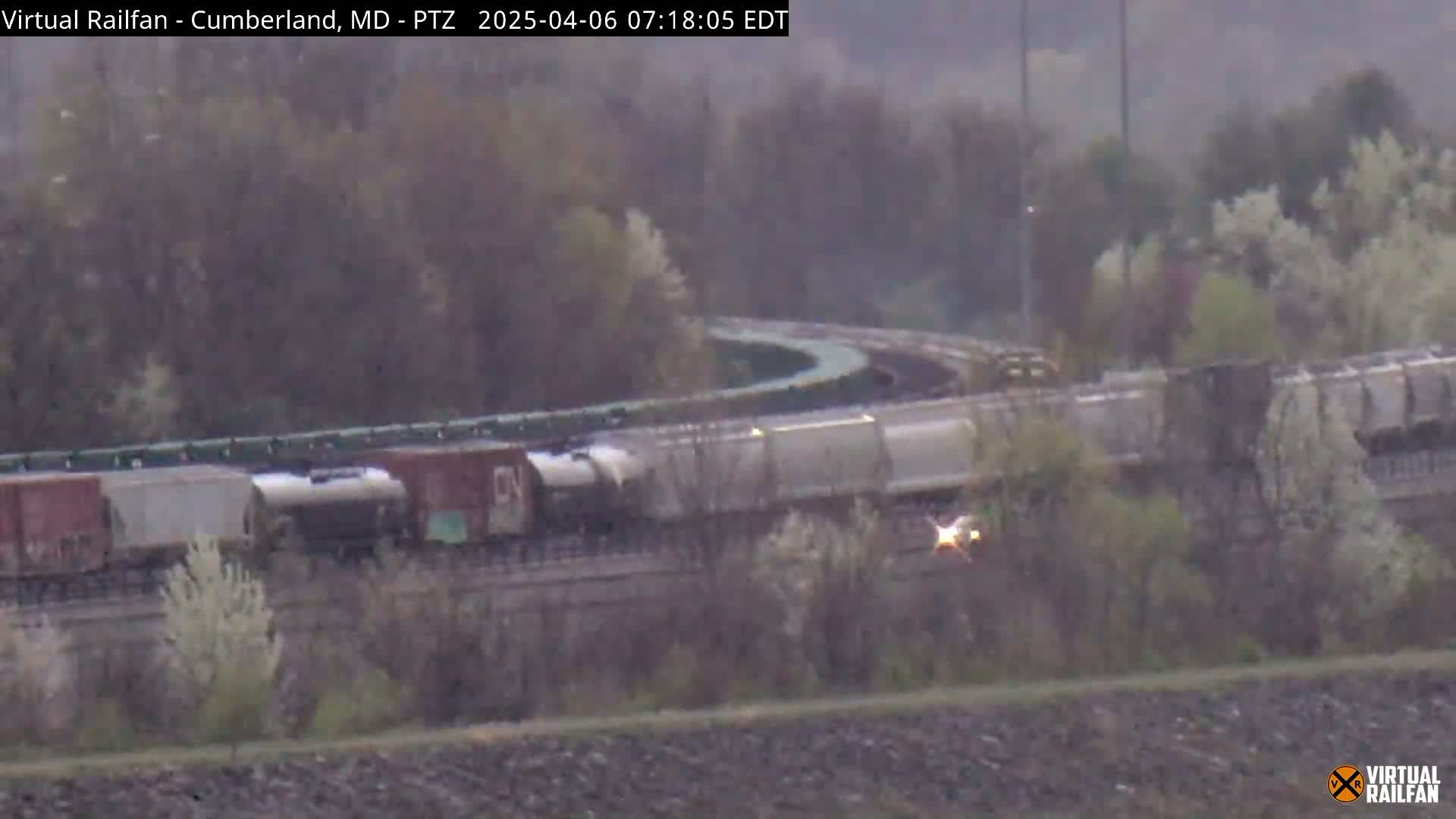 A long freight train rounds a curve on a track surrounded by hazy, spring vegetation.