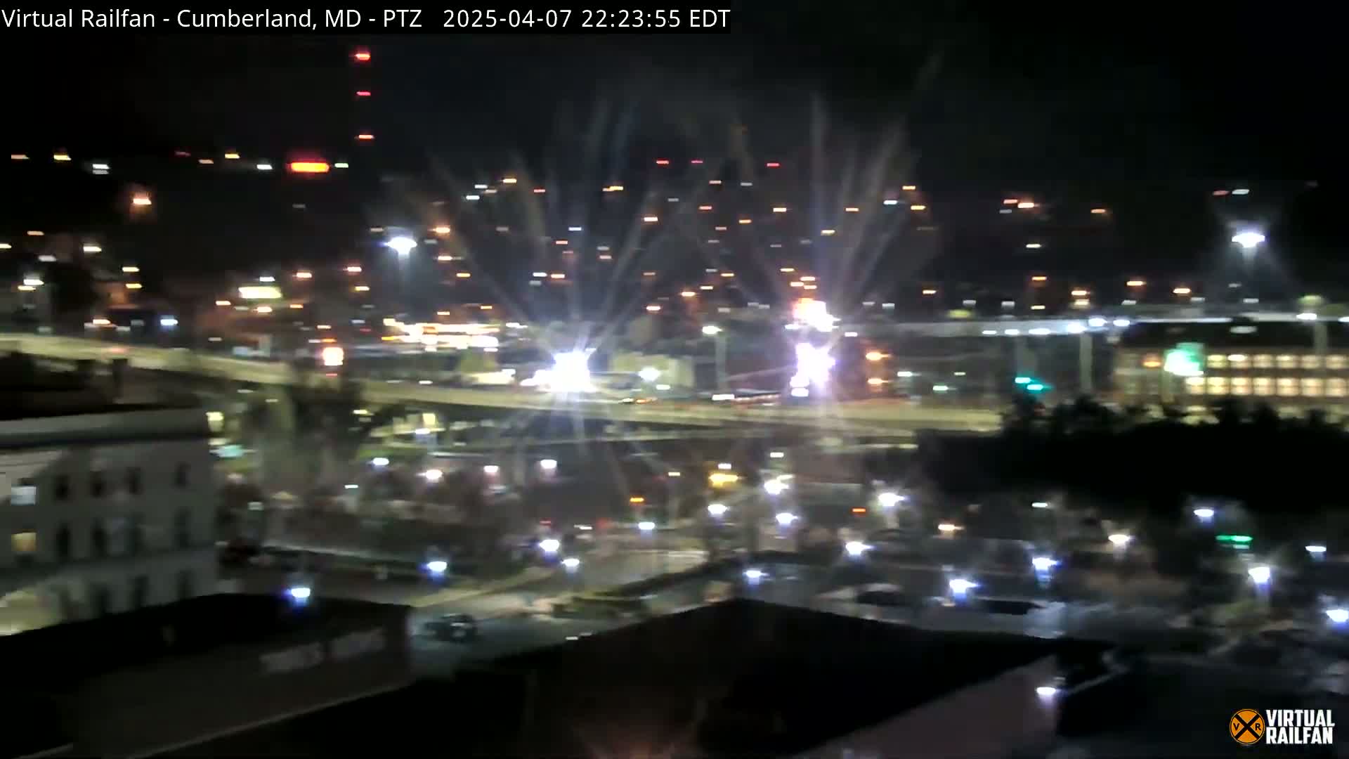 A nighttime, elevated view shows a highway interchange with numerous lights and vehicles, and some buildings in the foreground.