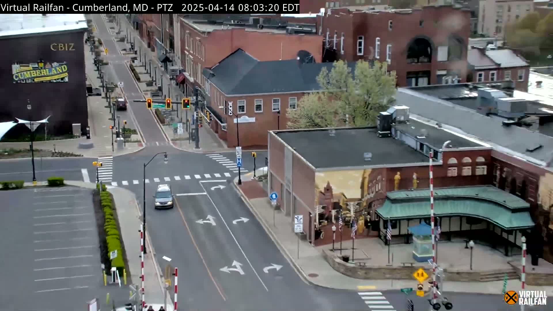 A mostly clear, daytime overhead view of a city street intersection with several brick buildings, a vehicle driving down the road, and a bike lane.