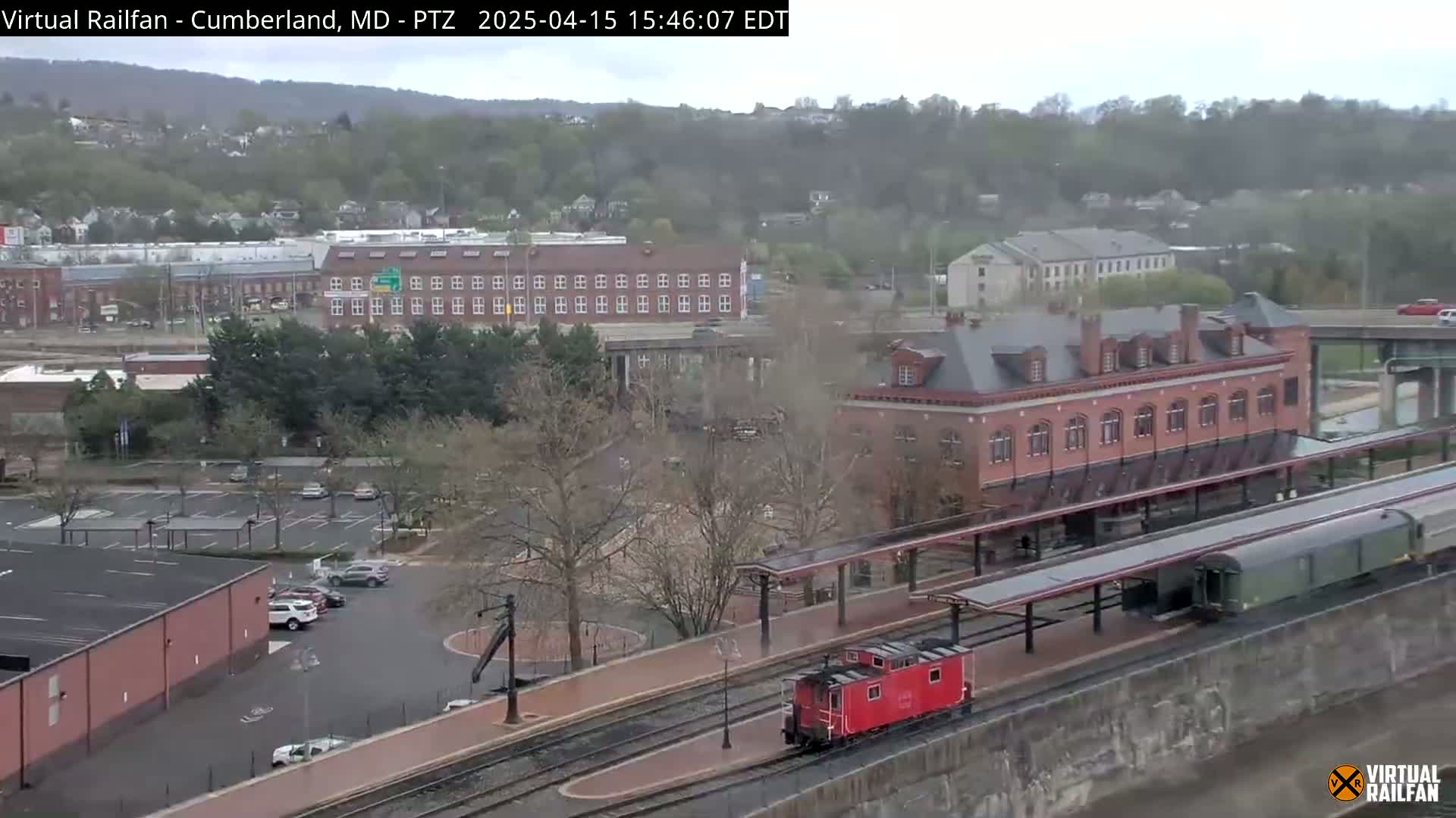 A red caboose and a long freight train sit at a station in a town on an overcast day.
