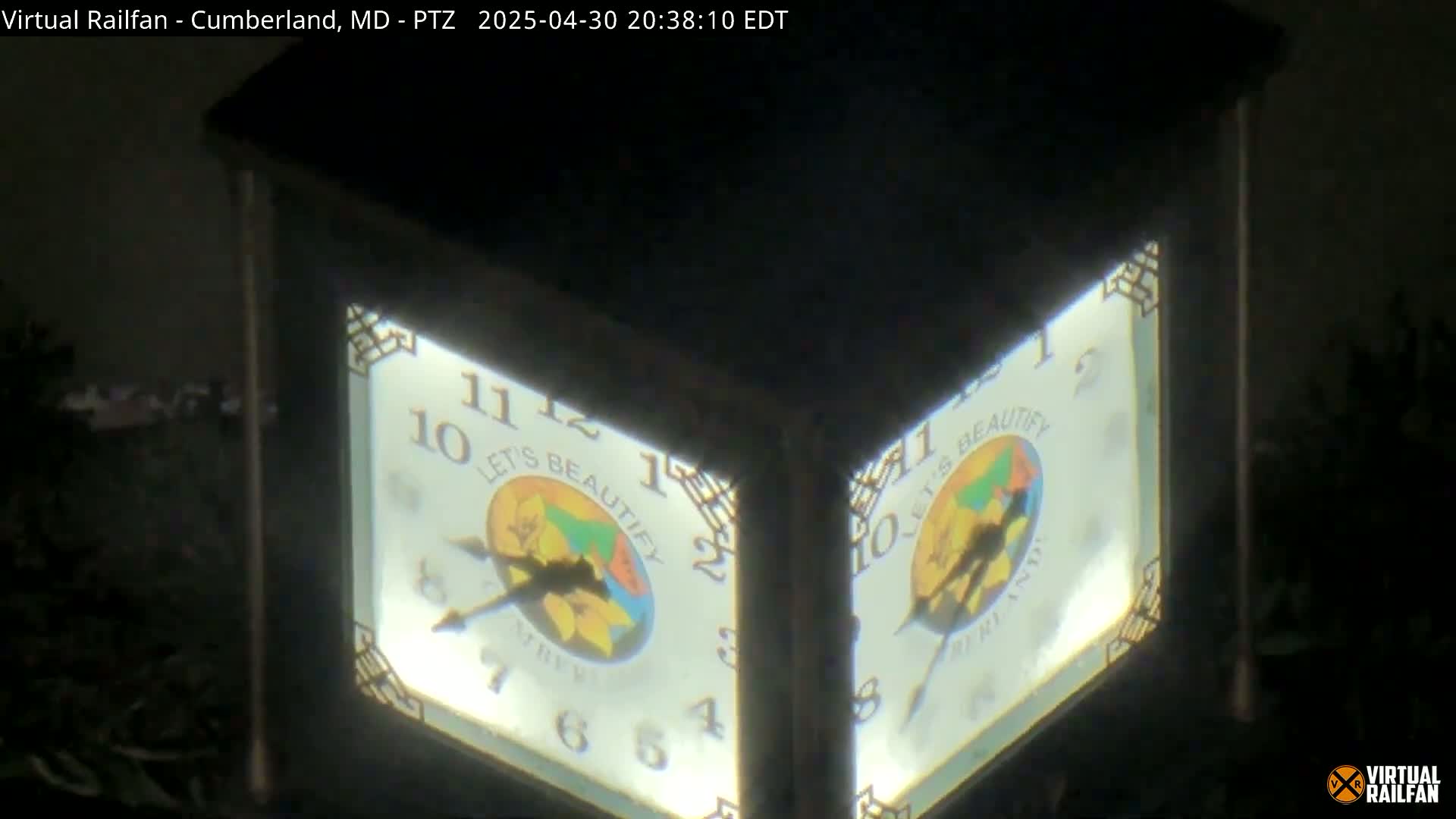 A nighttime close-up shows a double-sided illuminated clock with a circular design featuring the words "Let's Beautify."