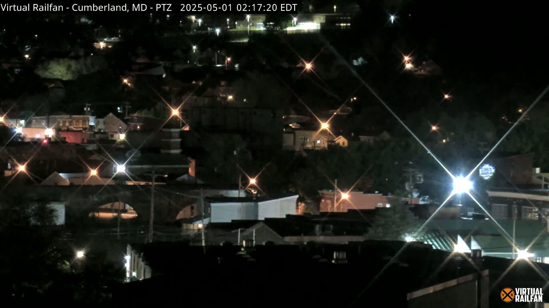 A nighttime, long-range view of a town, showing numerous houses and buildings with lights glowing.