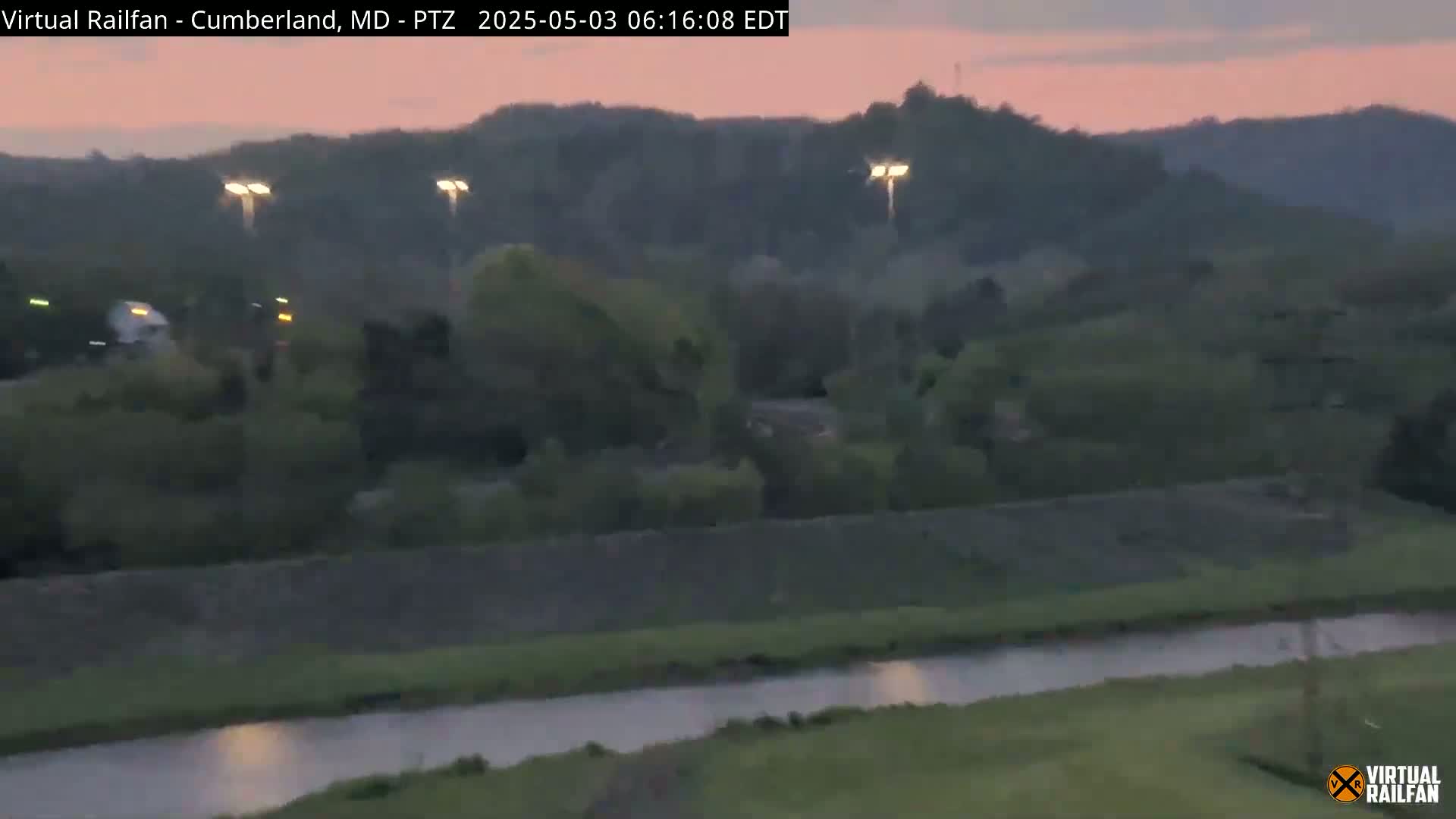 A tranquil river flows through a verdant landscape at dusk, under a pinkish-grey sky.