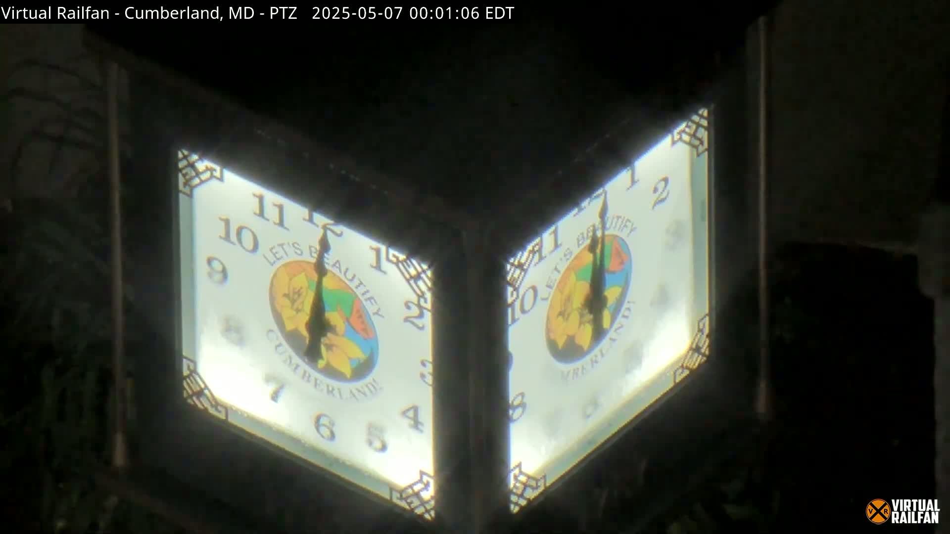 A nighttime close-up shows two illuminated clock faces mounted on a dark structure, each displaying a circular logo.
