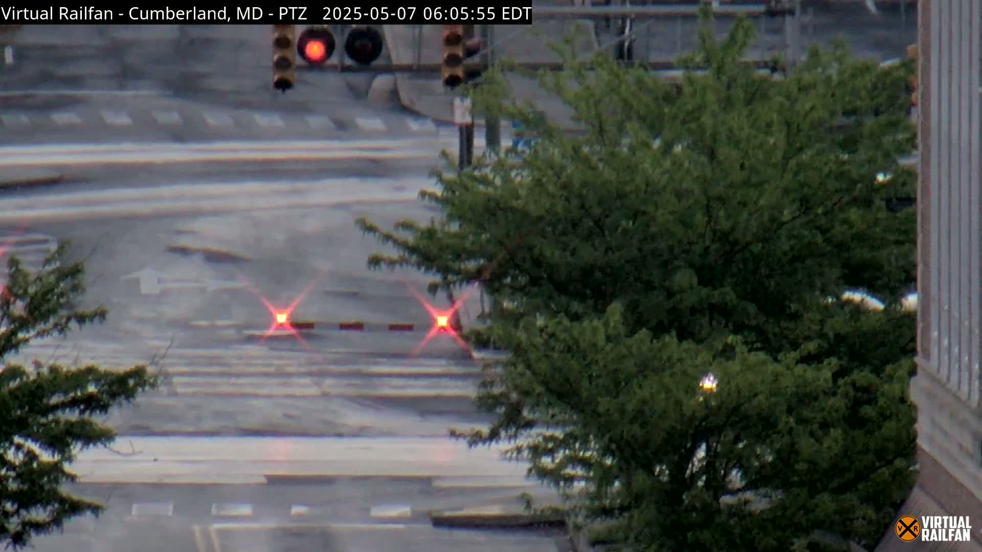 A wet street intersection with traffic lights and green trees is visible on an overcast day.