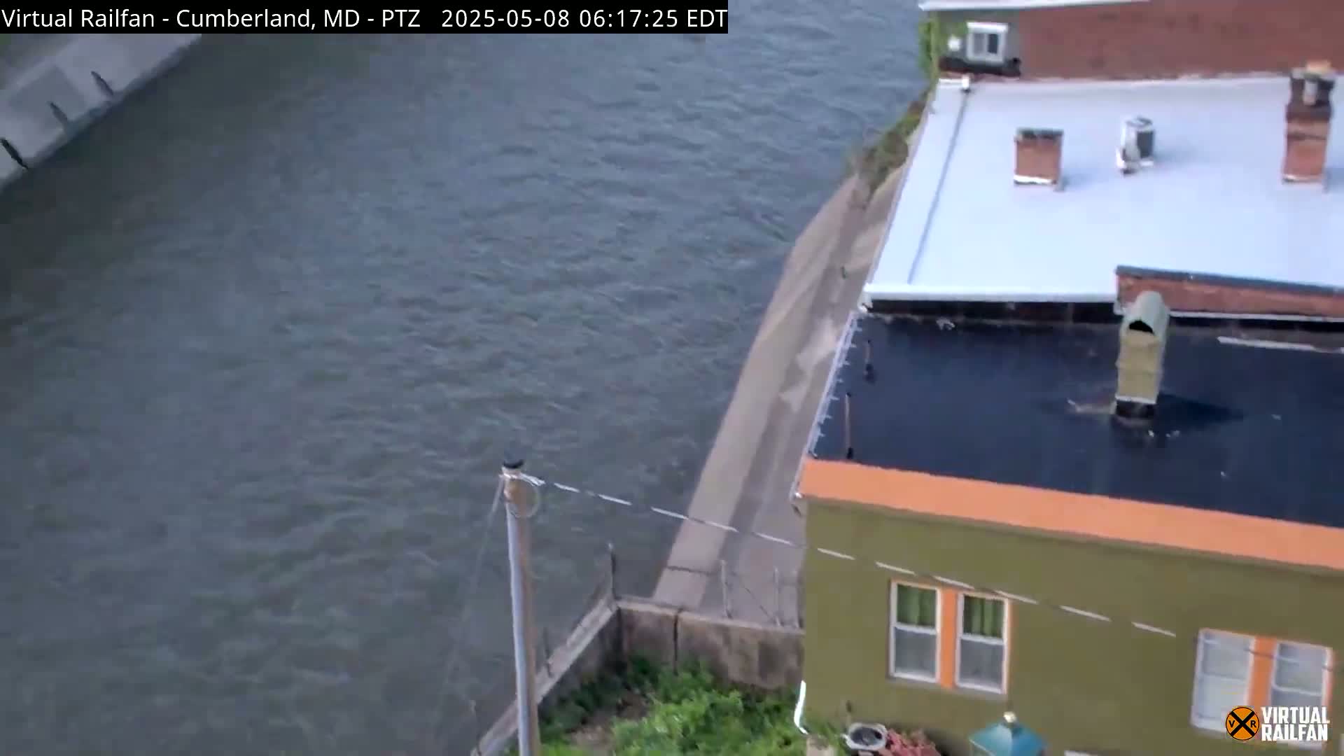 A mostly calm body of water borders a green building with an orange trim and a flat roof, under a partly cloudy sky.