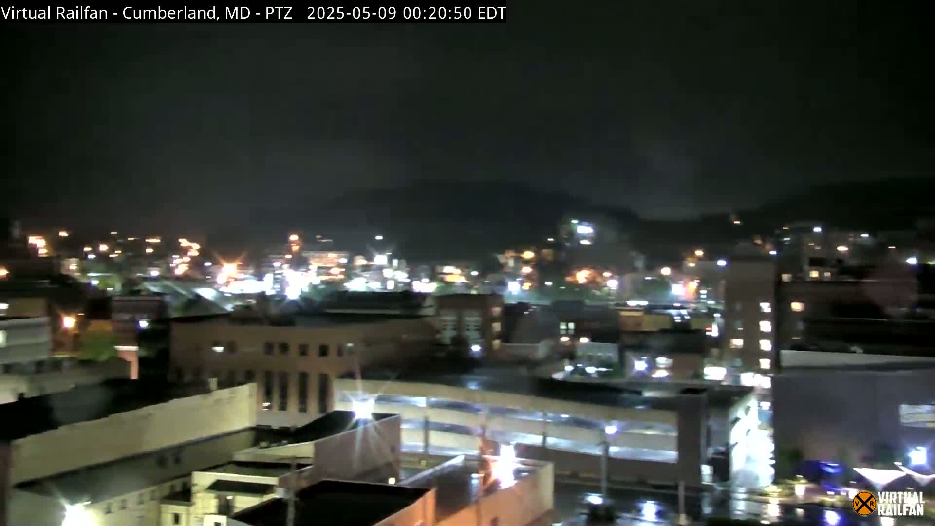 A nighttime view of a city with illuminated buildings and streets under a dark, possibly rainy sky.