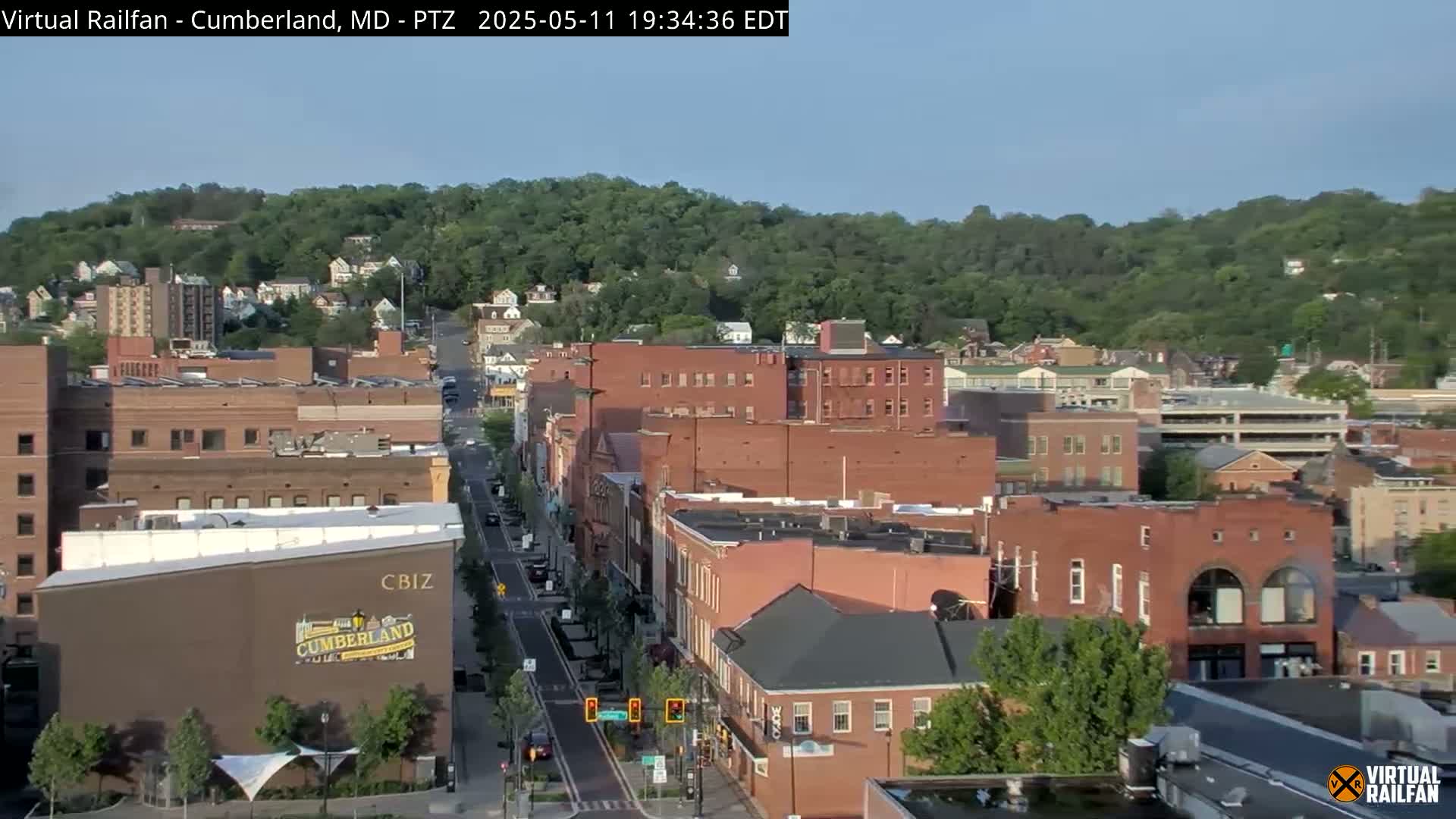 A mostly sunny view of a city street lined with brick buildings, nestled beneath a green hill.