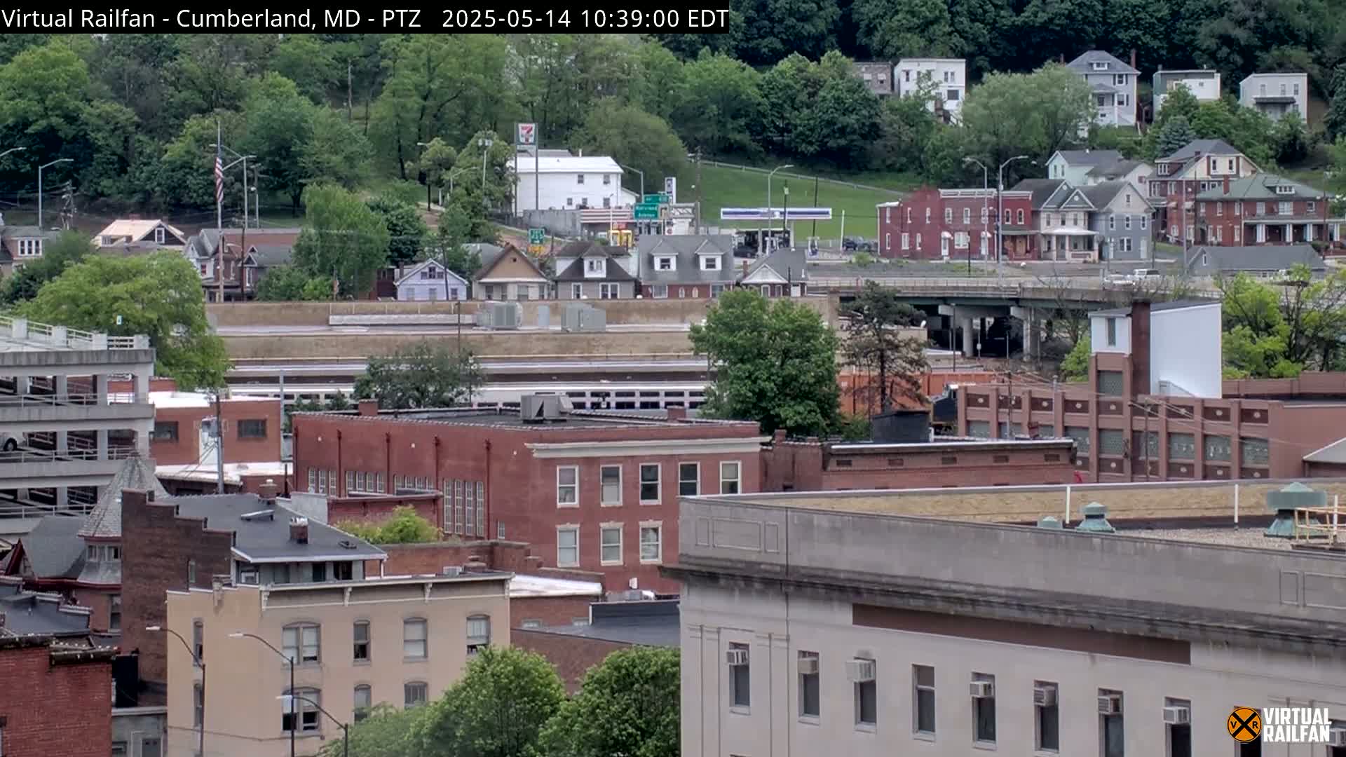A view of a city on a partly cloudy day, showing a mix of residential houses and brick buildings, with a train visible in the distance.