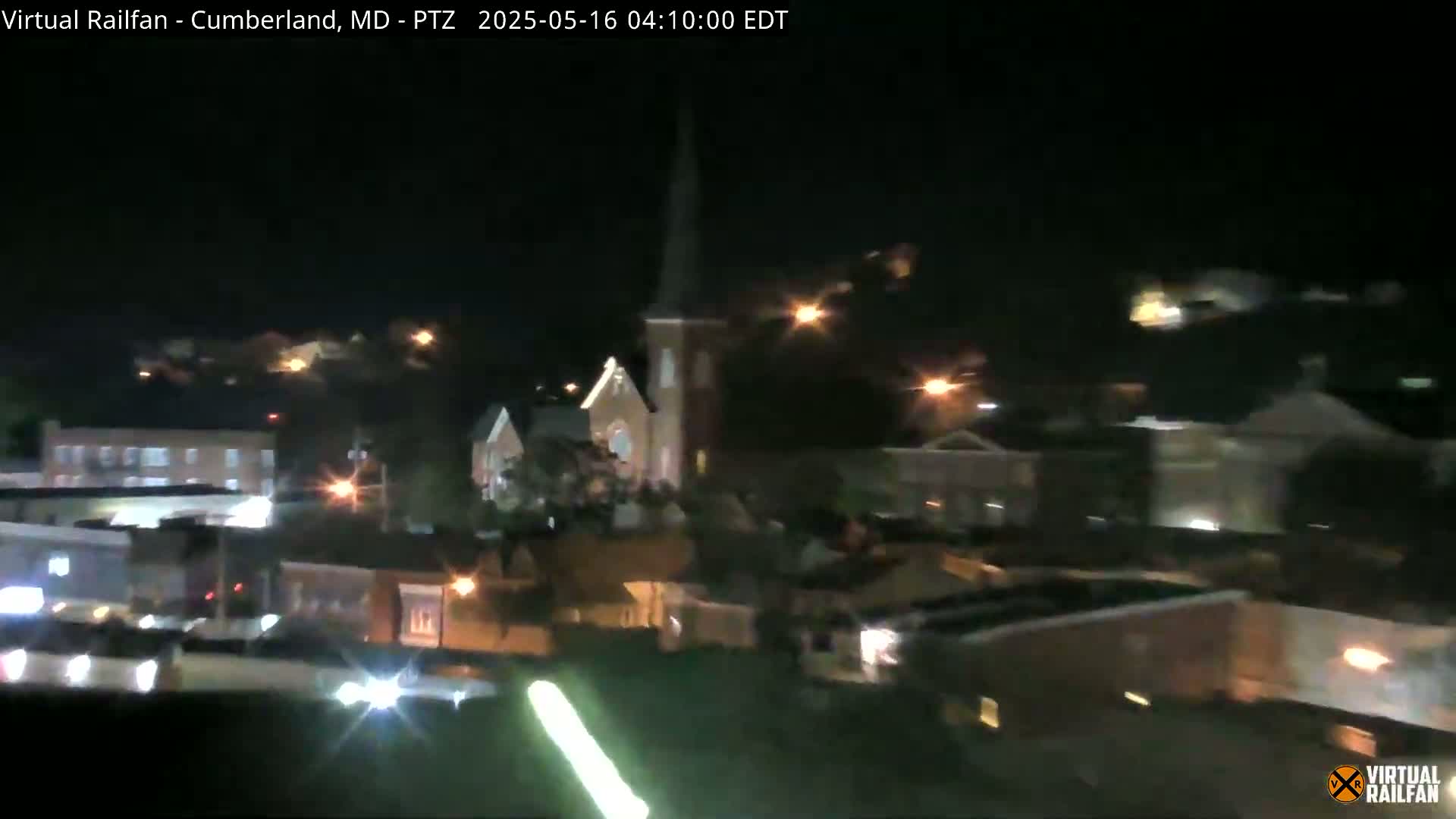A nighttime view of a small town with a church steeple visible among other buildings, under a clear, dark sky.