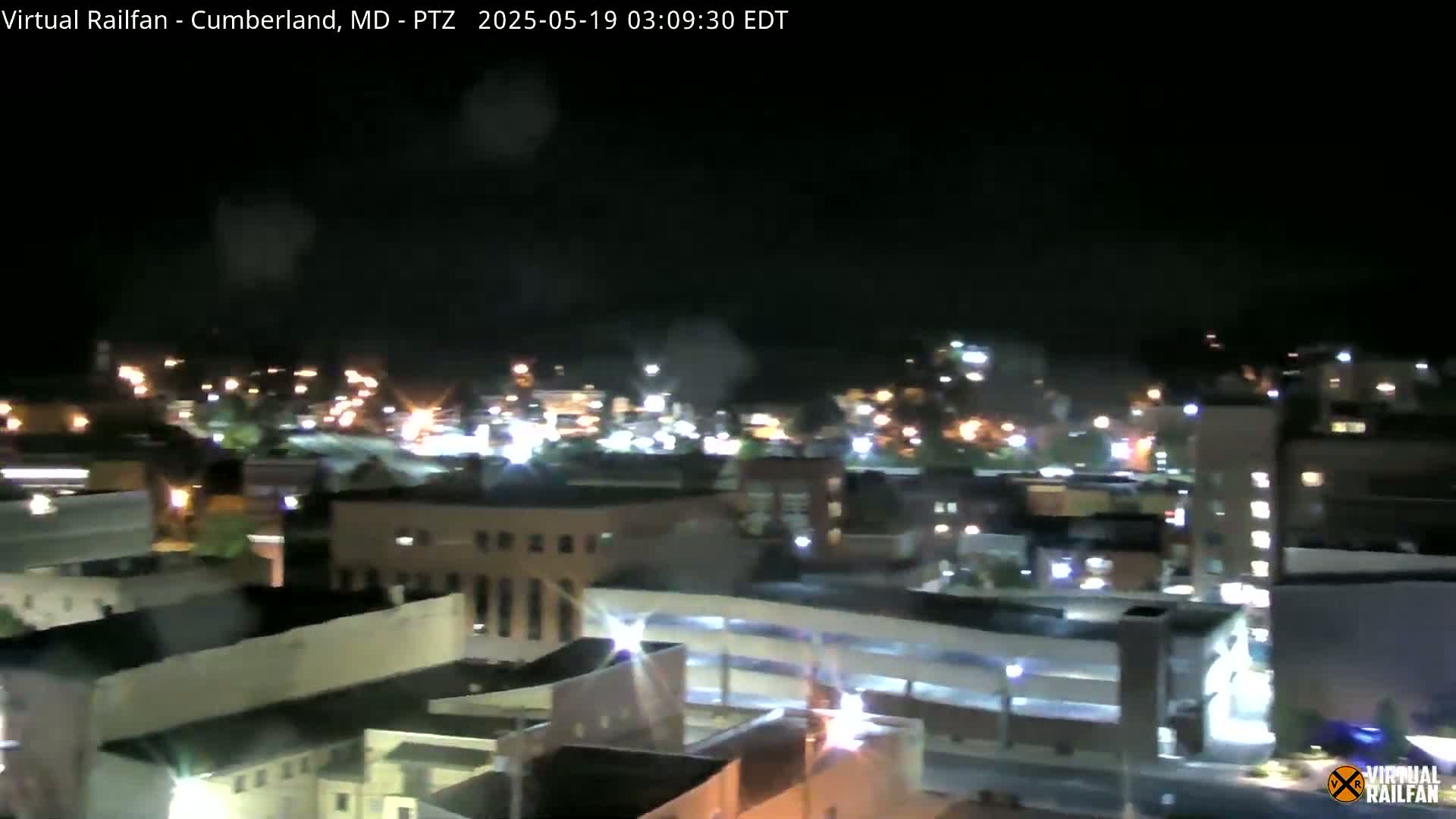 A nighttime, possibly rainy, long shot of a city with illuminated buildings and streets.