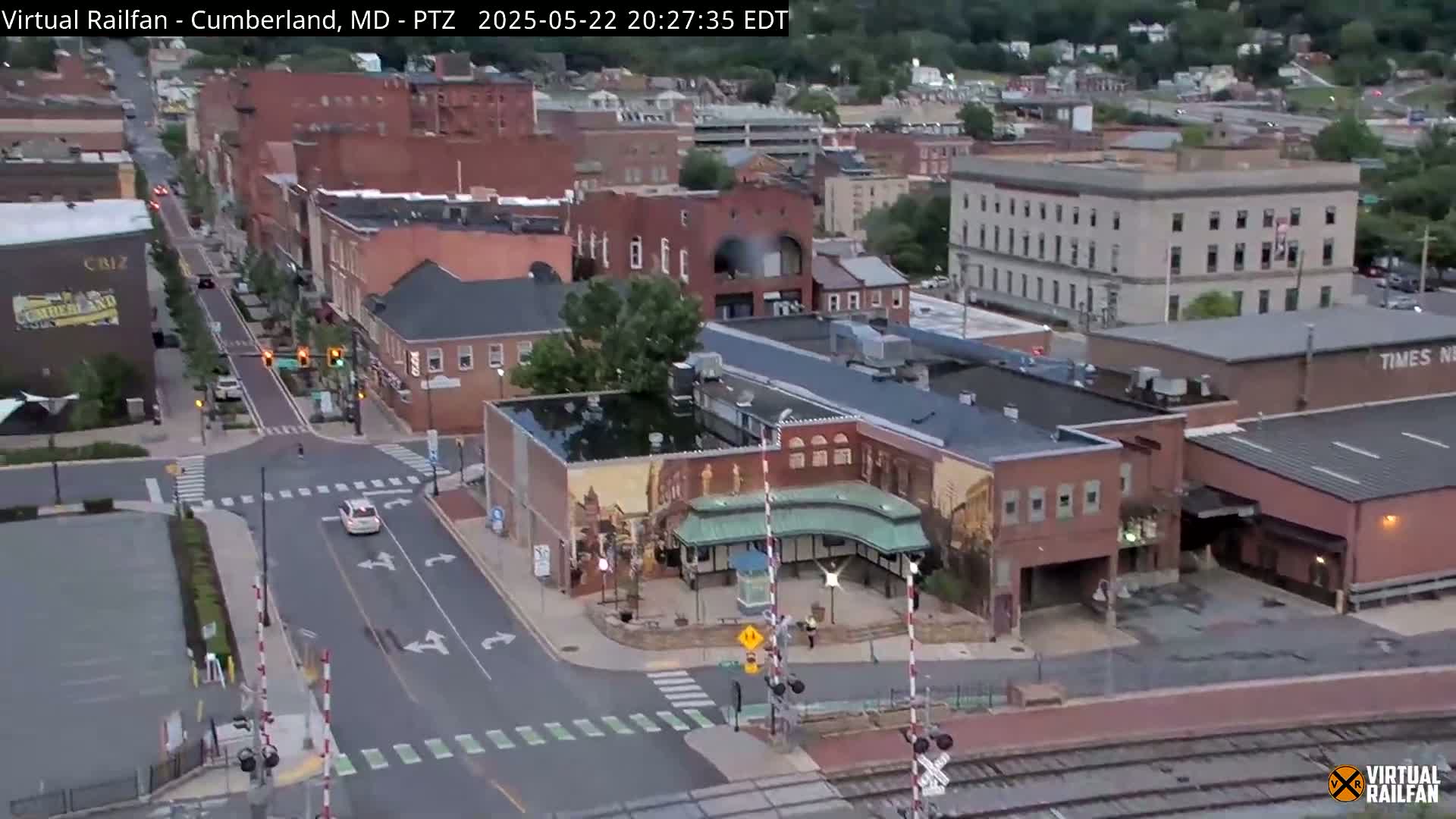 An aerial view of a town at dusk, showing streets, brick buildings, and a railway crossing.
