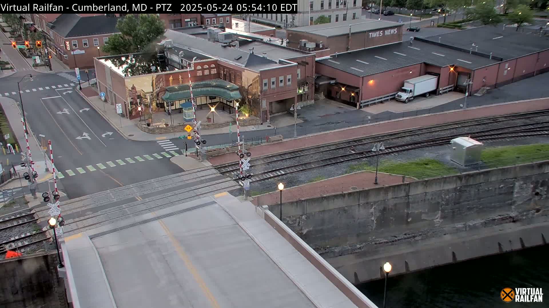 A high-angle view of a city intersection with railroad tracks, a bridge, and a canal, under twilight conditions.