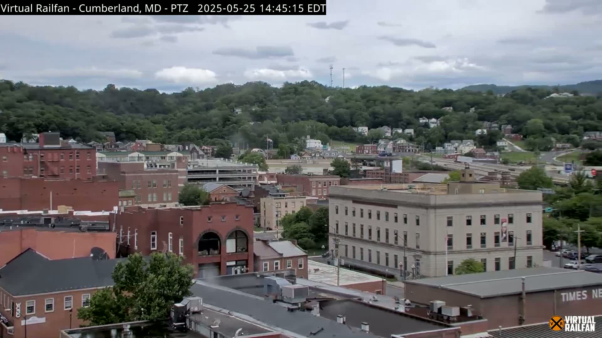 A partly cloudy day reveals a cityscape of brick buildings nestled against a verdant hillside.