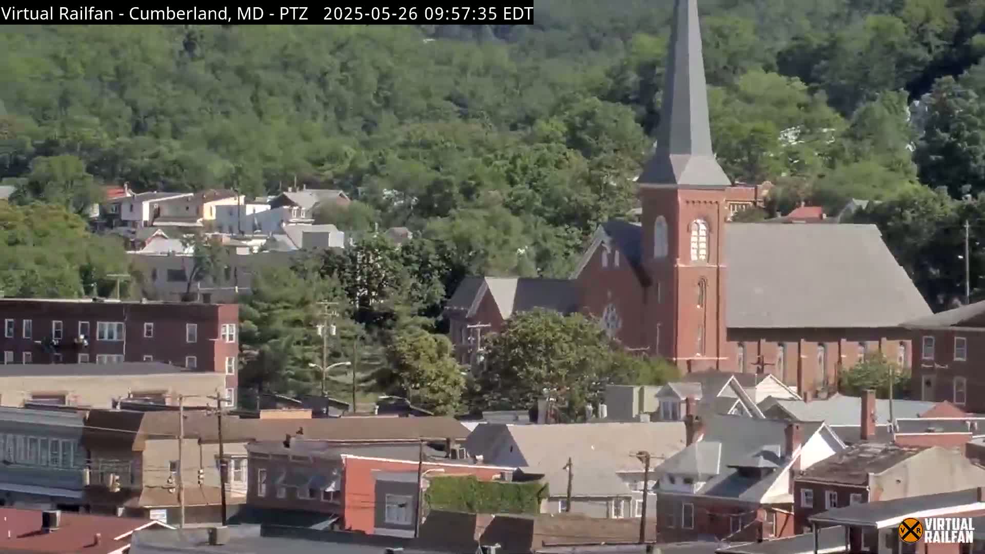 A brick church with a tall steeple is prominently featured in a residential area on a partly sunny day.