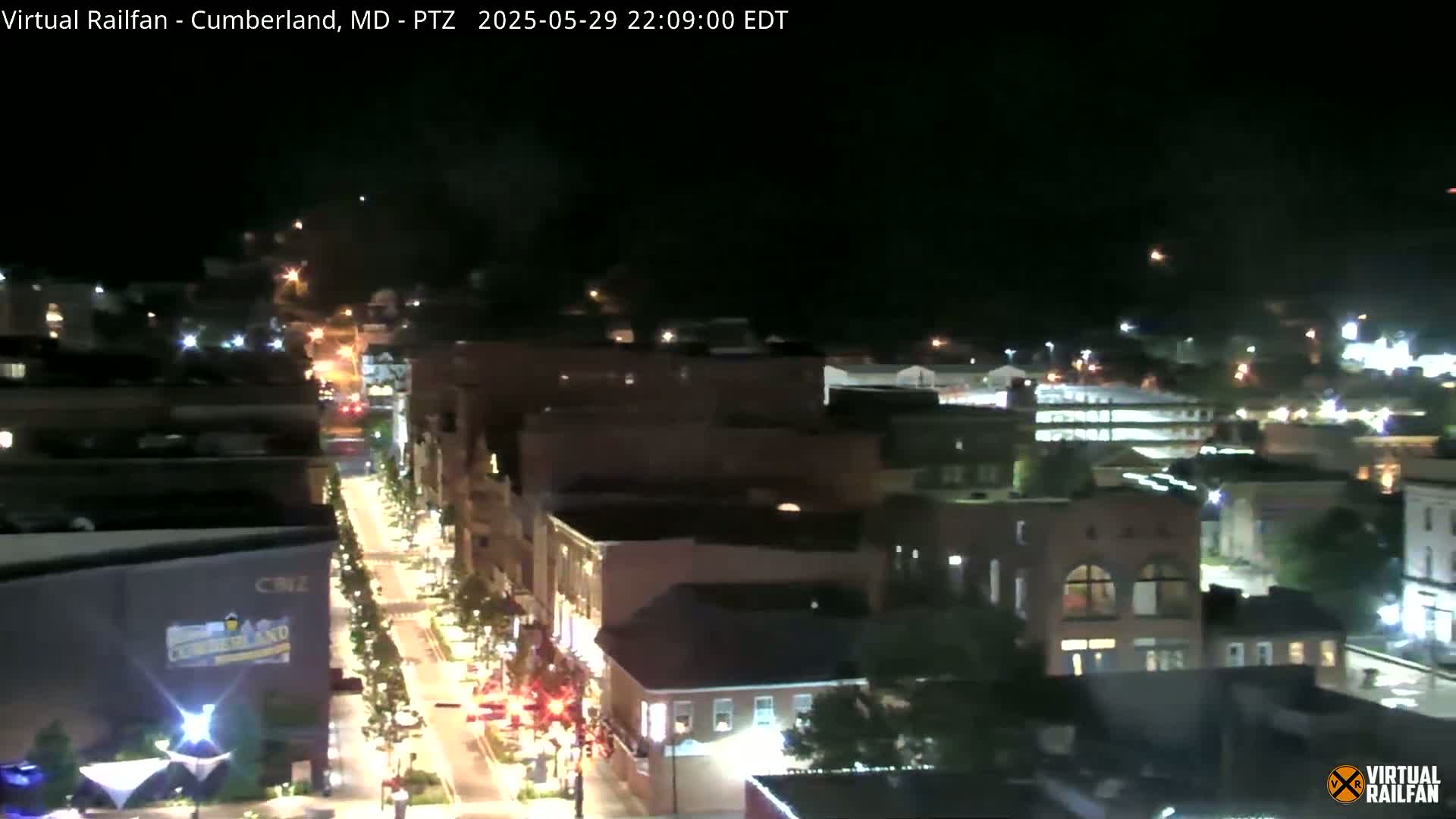 A nighttime, overhead view of a city street with buildings illuminated by streetlights and some vehicle lights.