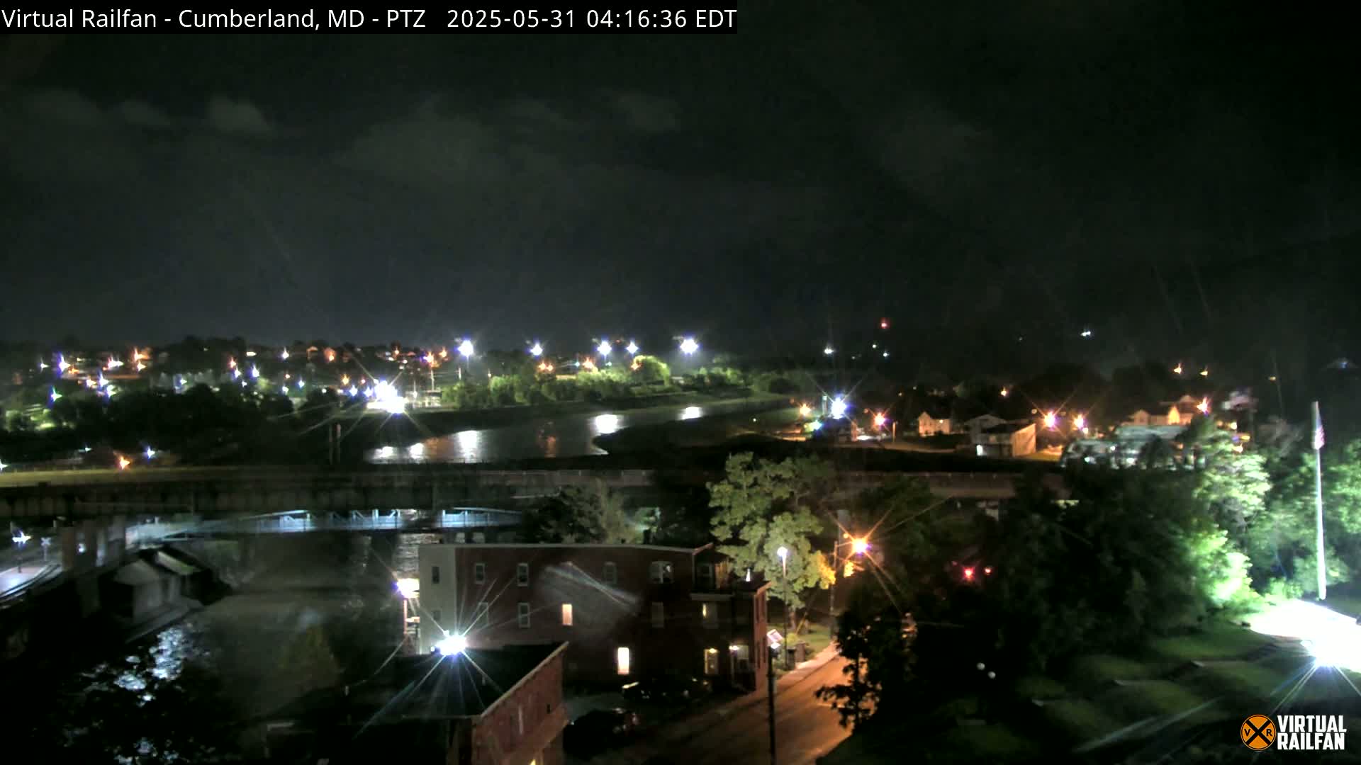 A nighttime view of a town with a river, bridges, and streetlights, under a partly cloudy sky.