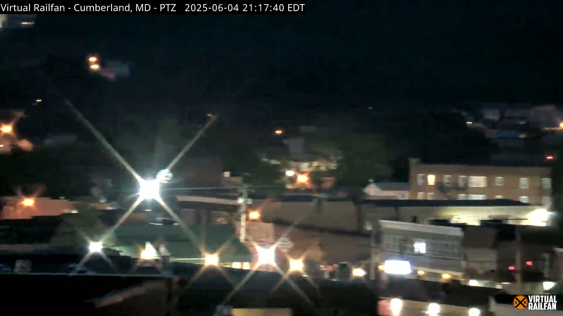 A nighttime long shot of a town, showing illuminated buildings and streets.