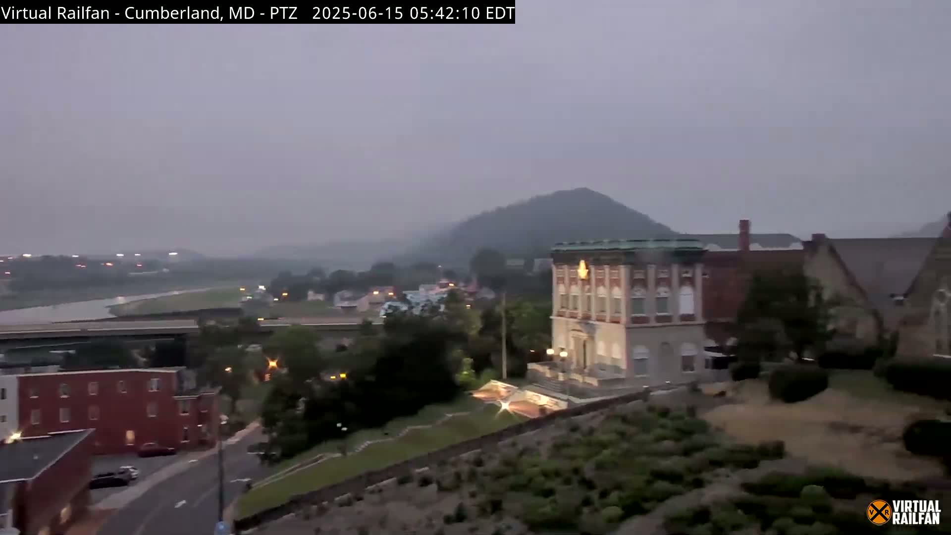 A hazy, overcast view of a town situated beside a river, with hills and buildings in the background.