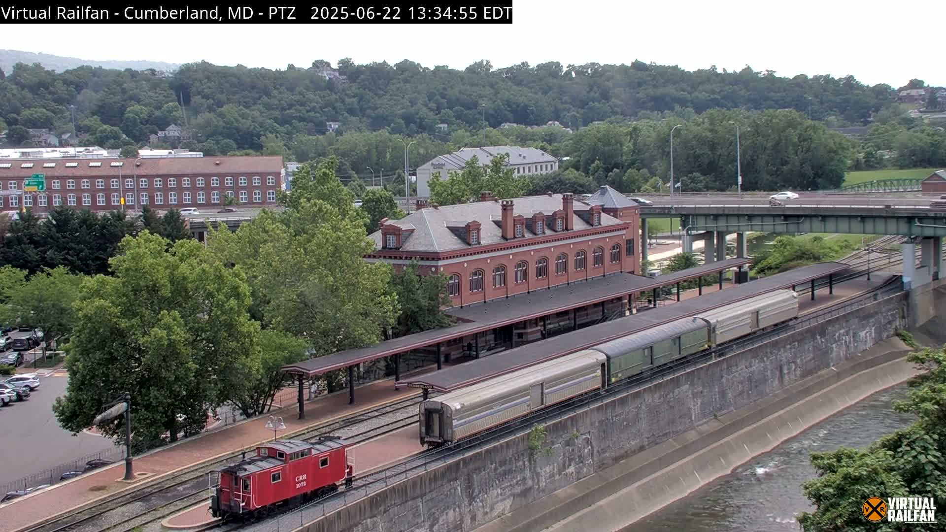 A passenger train sits at a station next to a river under a partly cloudy sky.