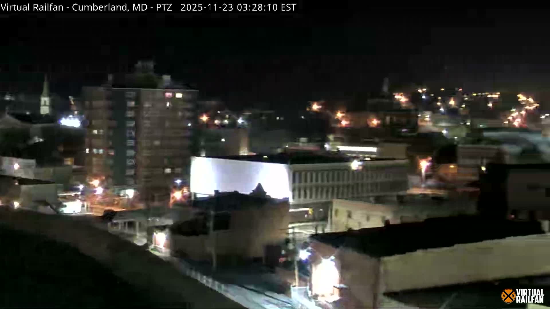 The image displays an urban landscape at night, featuring a mix of illuminated buildings and distant city lights under clear skies.