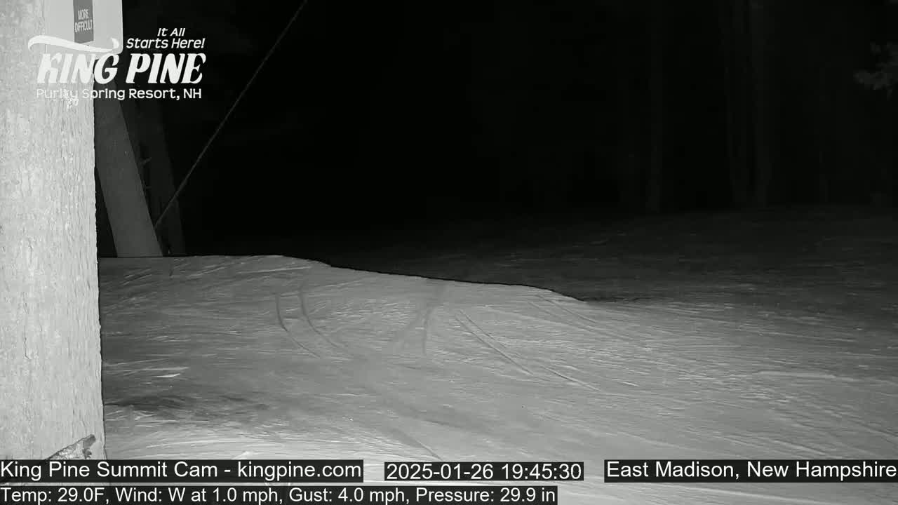 A nighttime, snow-covered scene shows a gently sloping expanse of snow under a dark sky.