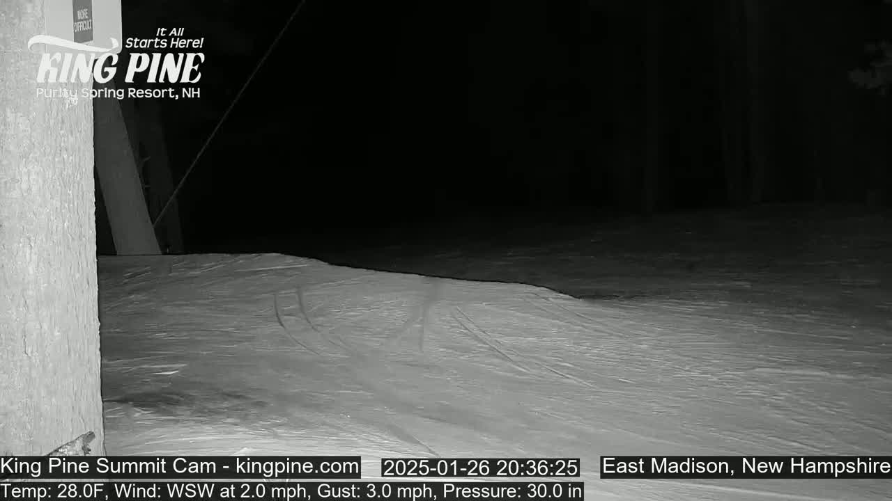 A nighttime, low-light image shows a snow-covered slope under a dark sky with a light wind.