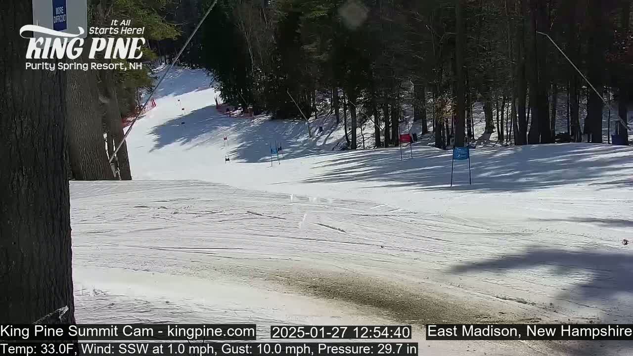 A snow-covered ski slope winds through a wooded area on a sunny day with a light south-southwesterly wind.