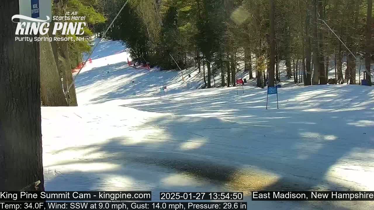 A snow-covered ski slope with trees in the background on a sunny day with a south-southwesterly wind.