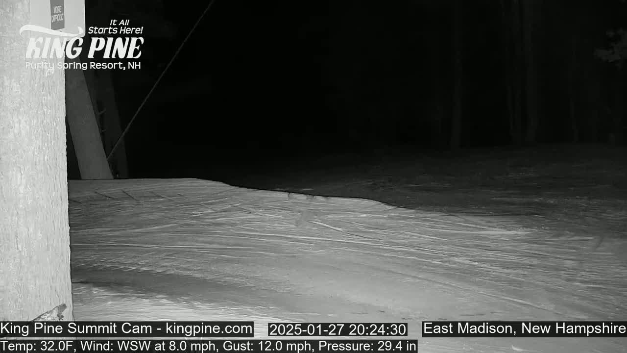 A nighttime view of a snow-covered slope with a dark forest in the background, under a dark sky with a temperature of 32°F, a wind from the west-southwest at 8 mph gusting to 12 mph.