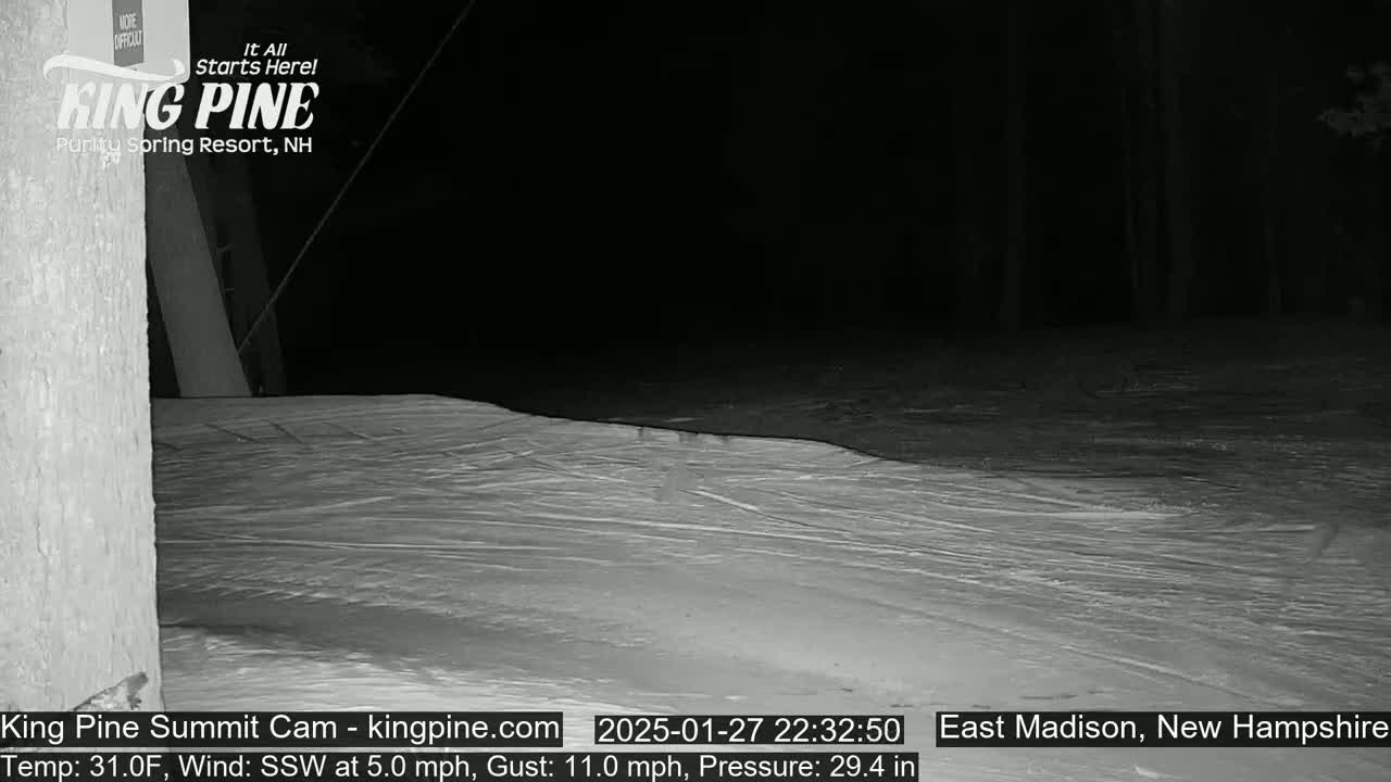 A snow-covered slope at night under a dark sky, with a slight wind.