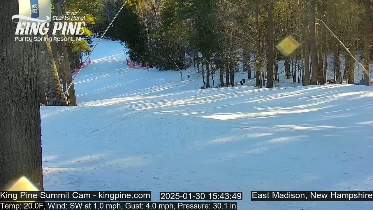 A snow-covered ski slope descends from a wooded area on a sunny day with a southwest wind.