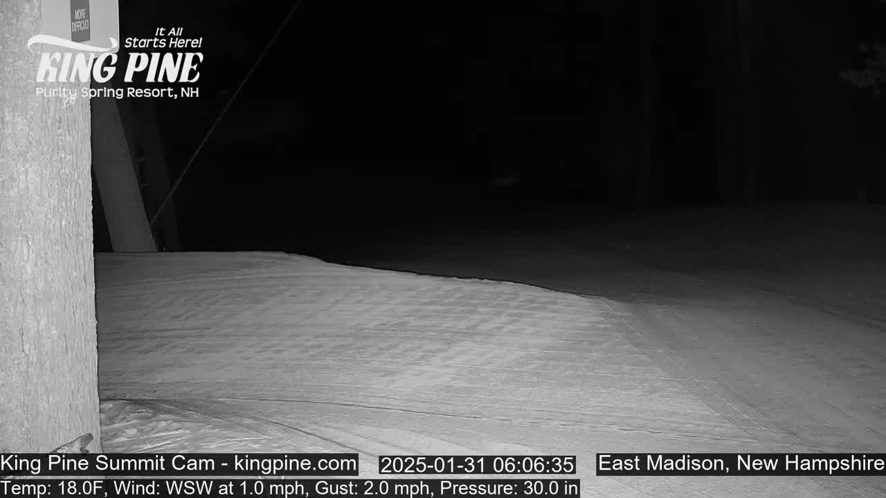 A snow-covered surface is visible at night, under a dark sky, with a portion of a building in the bottom left corner.