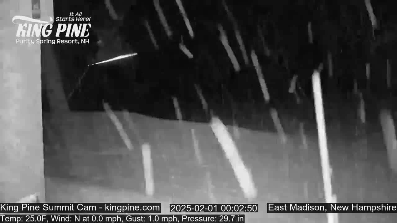 Snow falls at night in front of a building.