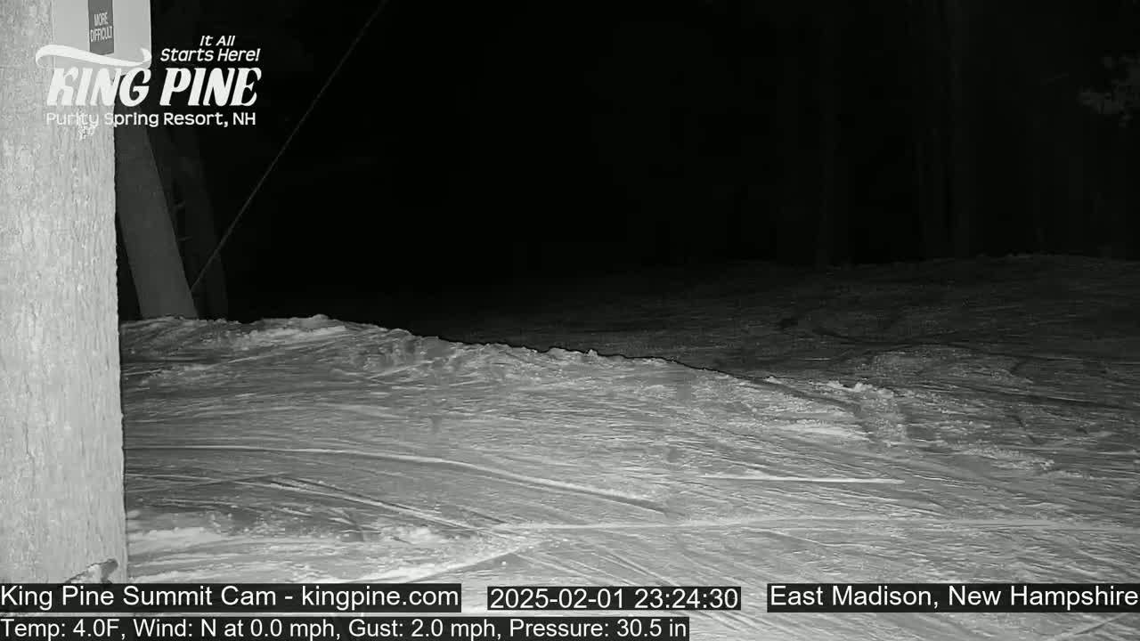 A nighttime view of a snow-covered slope with faint tracks, under a dark sky.