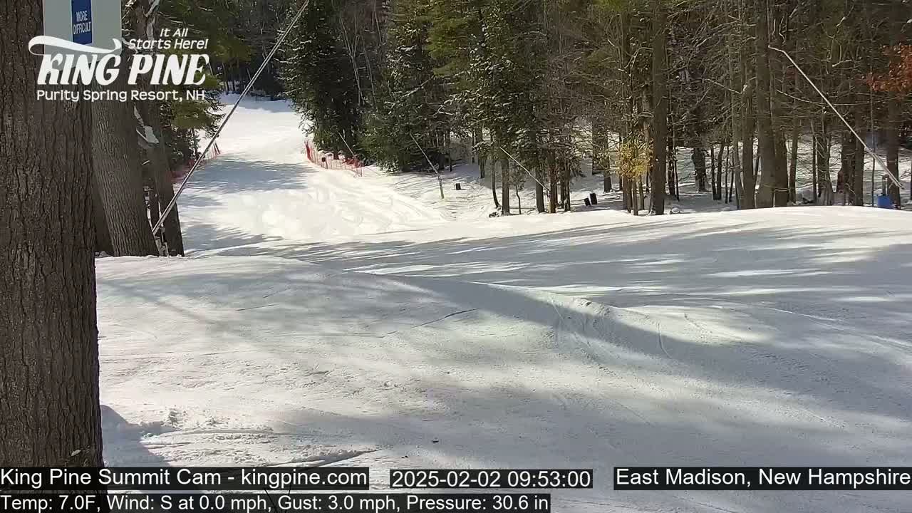 A snow-covered ski slope on a sunny day, surrounded by trees.