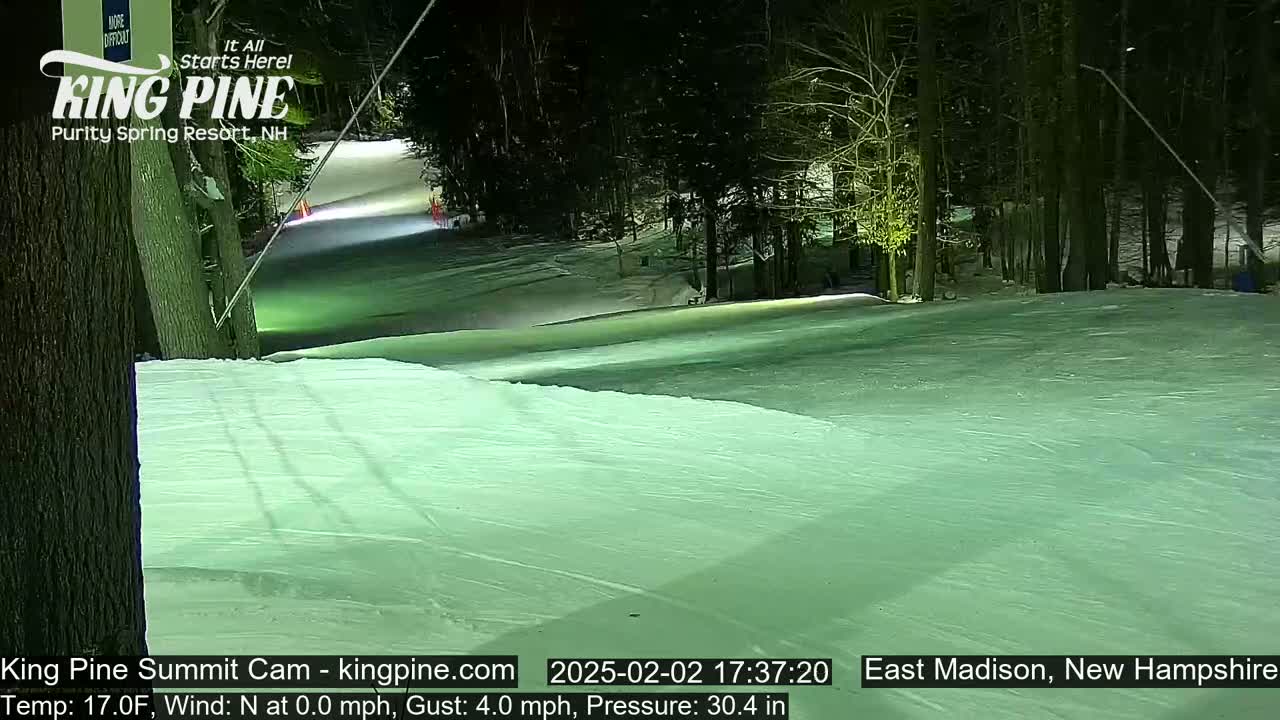 A snow-covered ski slope at night, illuminated by artificial lights, is surrounded by dark trees under a clear sky.